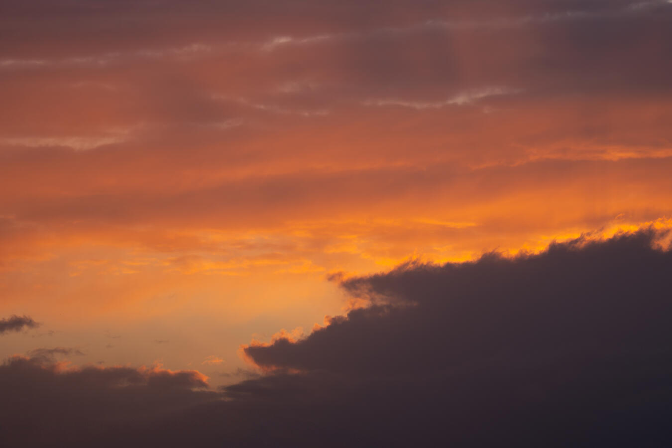 Nahaufnahme von Wolkenstrukturen während eines Sonnenuntergangs in Porta Westfalica. Der Himmel zeigt einen Farbverlauf von tiefem Orange zu Pfirsich, durchbrochen von einer massiven, dunklen Wolke im unteren Vordergrund.