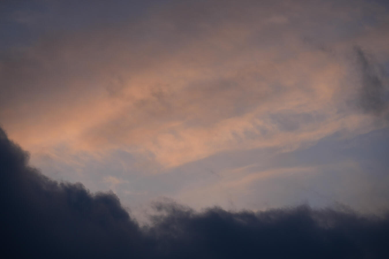 Detailaufnahme atmosphärischer Phänomene in Porta Westfalica. Weiche, pfirsichfarbene und rosafarbene Wolken im späten Tageslicht stehen im Kontrast zu den massiven, dunklen Gewitterwolken im unteren Teil des Bildes.